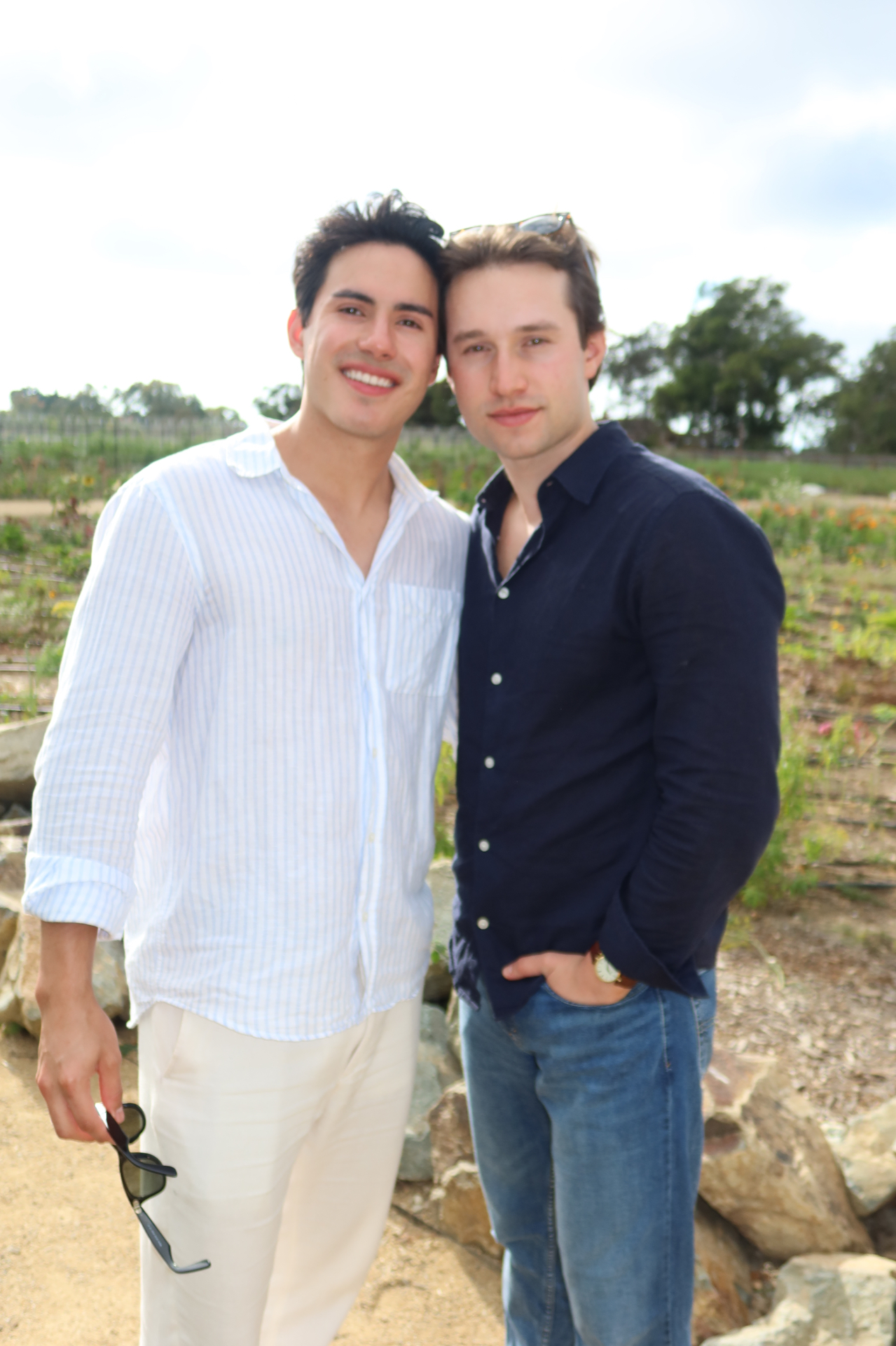 Griffin and Neiyell smiling together at a vineyard in linen shirts