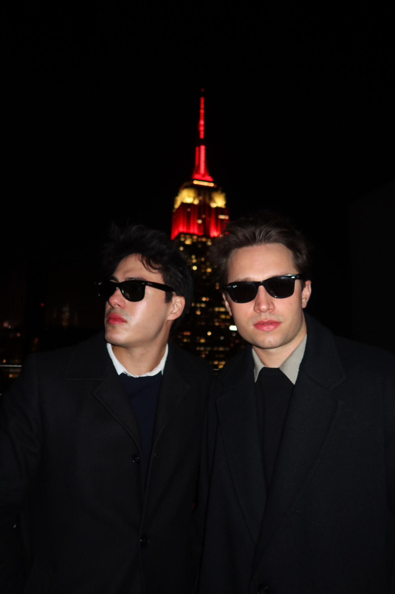 Griffin and Neiyell in black overcoats at night with the Empire State Building behind them