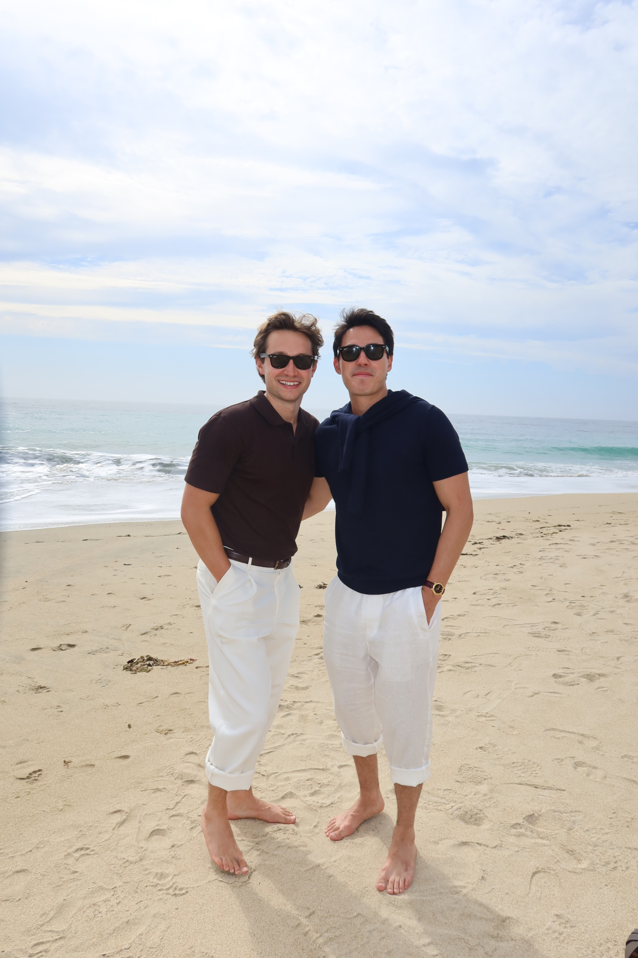 Griffin and Neiyell barefoot on the beach in white linen trousers